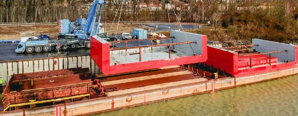 Crane loading a red floating dock section onto a barge